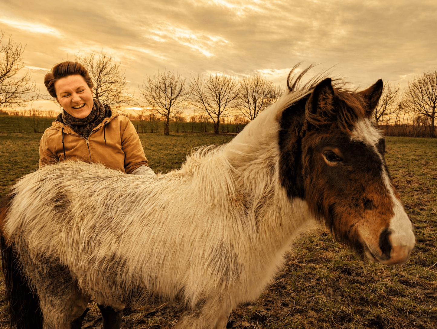 A woman resting her hand on a horse in an open pasture